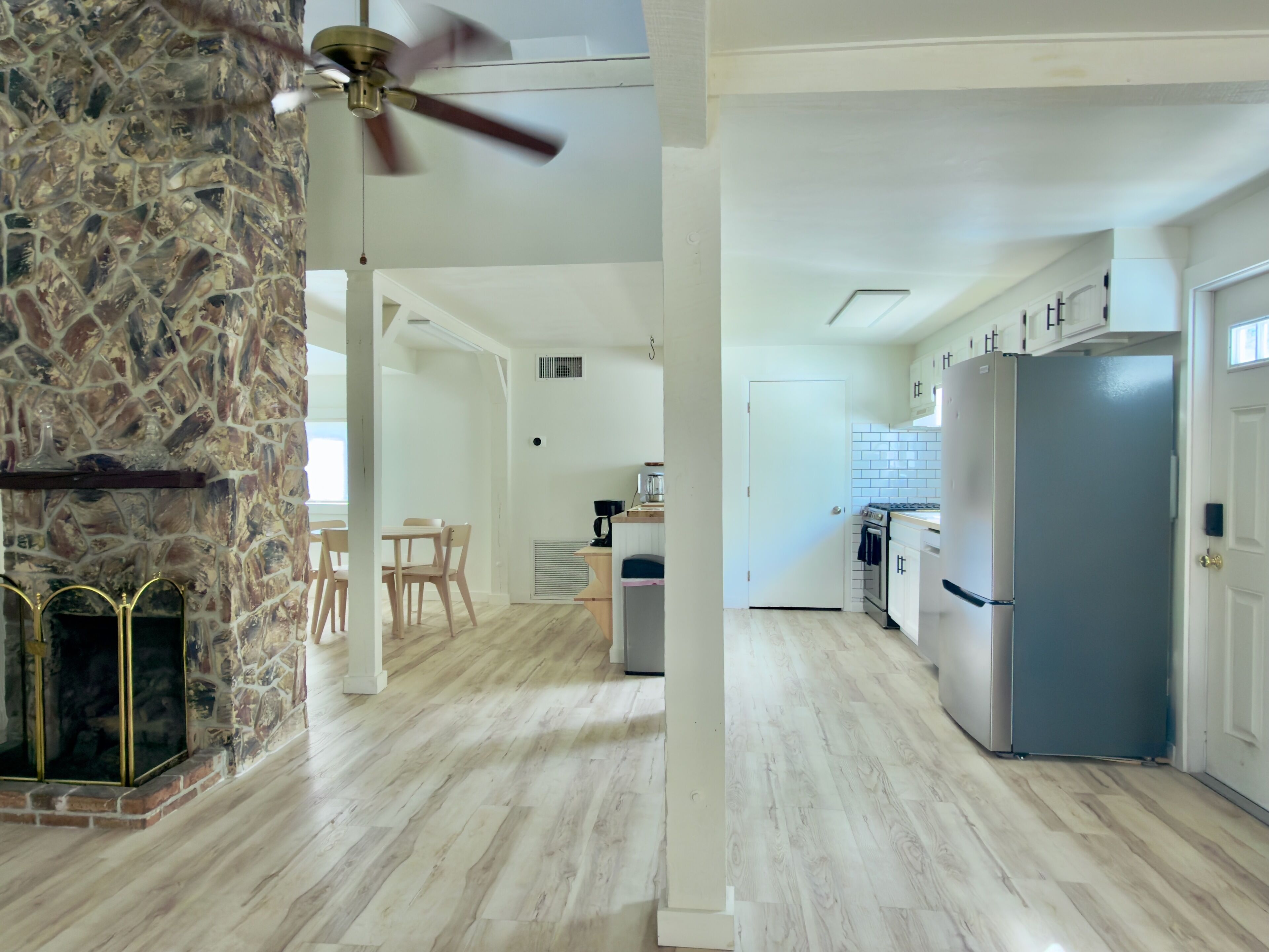 A spacious kitchen with a stone wall, wooden floor, and a modern refrigerator.