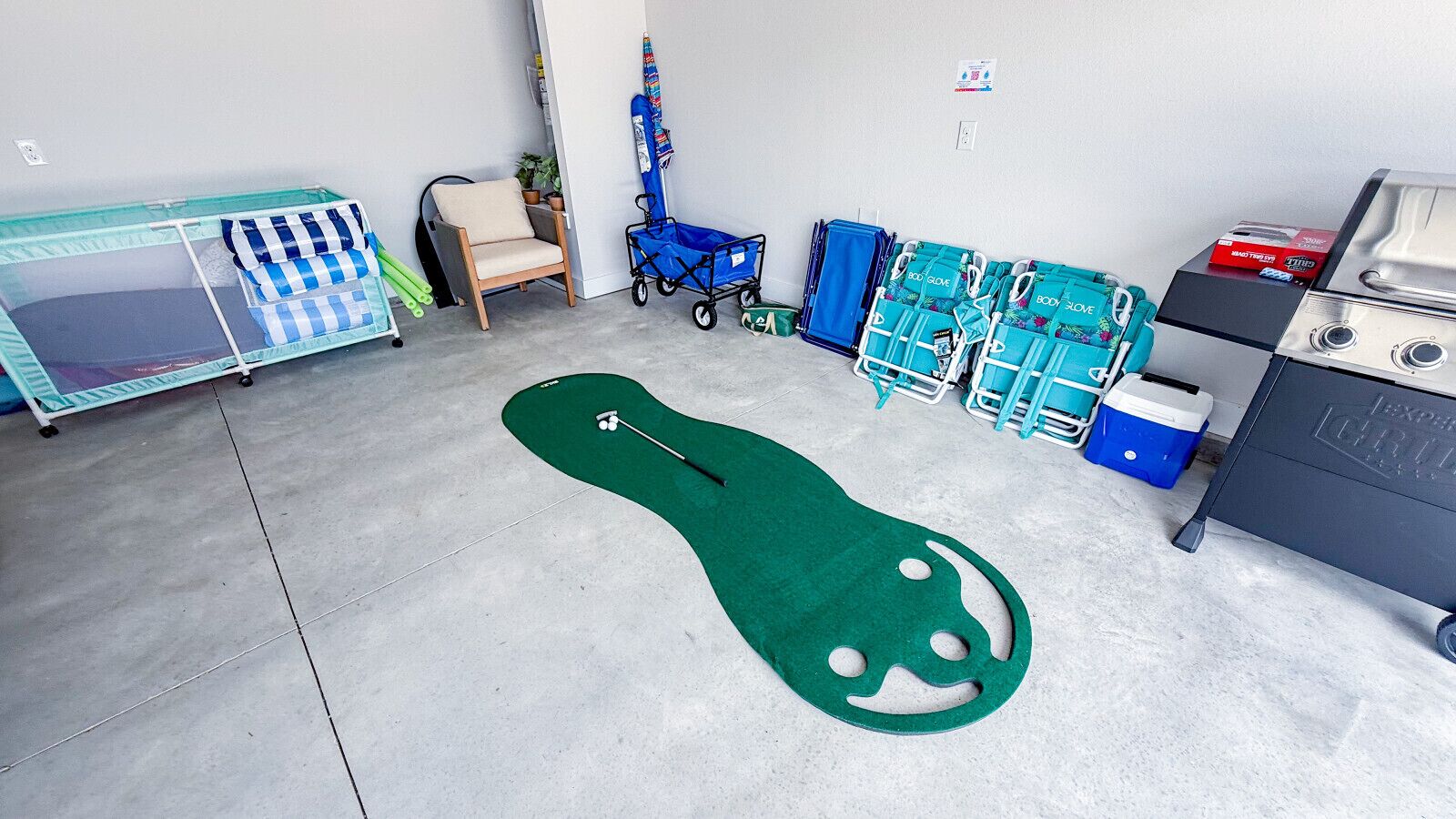 A room with a green mat, a crib, a stroller, and a cart with blue bags.