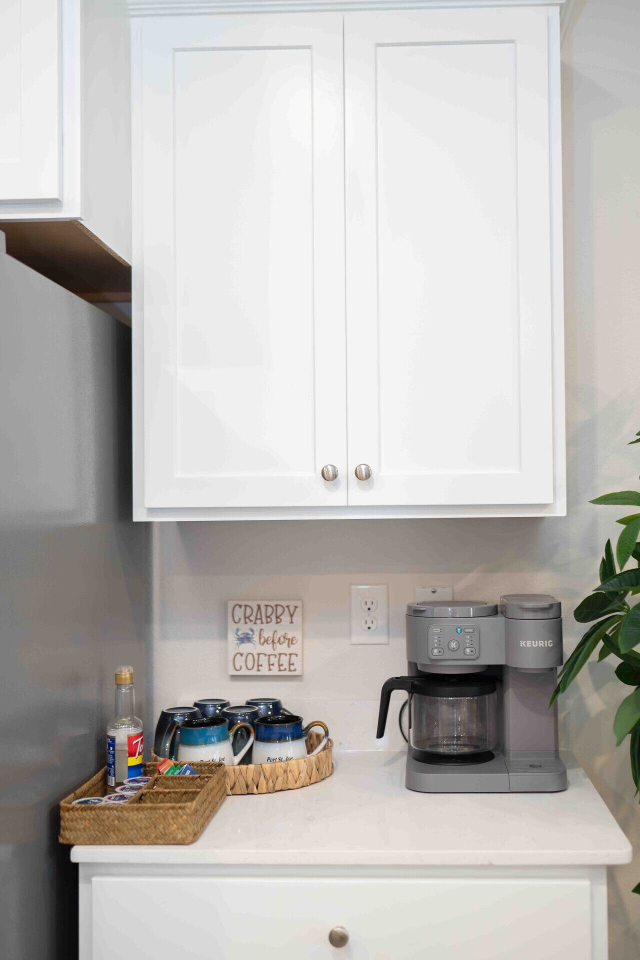 Een kitchenette met een koffiezetapparaat, een bordje met de tekst 'CRABBY voor koffie' en een mandje koffiekapsules.