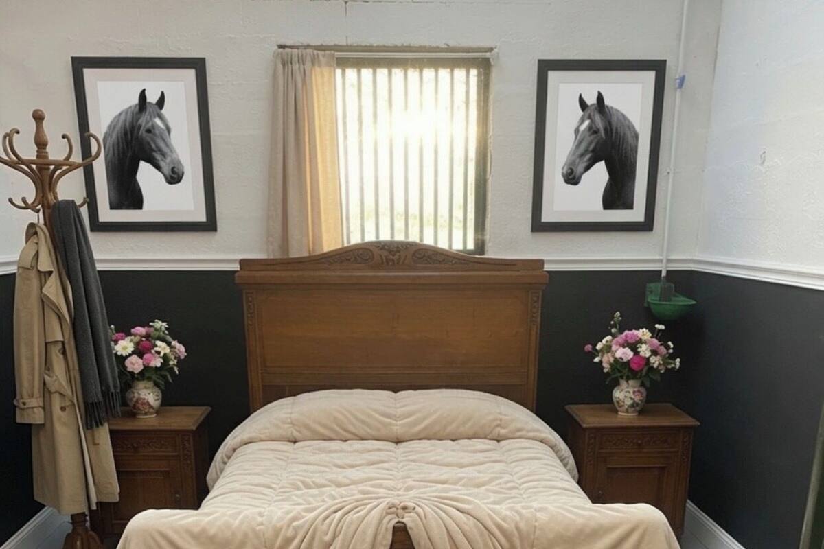 Un lit avec une tête de lit en bois, deux tables de chevet ornées de vases de fleurs et deux portraits de chevaux encadrés accrochés au mur.