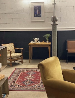 A room with a dark wall, a framed picture, a wooden table with a teapot, cups, and a plant, a patterned rug, a yellow armchair, and a wooden chair. - Domaine de la Pause enchantée (Saint-Guinoux)