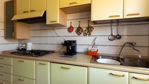 Cozinha com armários amarelos, fogão a gás, cafeteira e utensílios de cozinha pendurados.