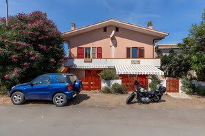 Ein zweistöckiges Haus mit Satellitenschüssel, einem roten Auto und einem Motorrad vor der Tür.