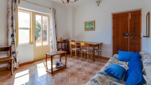Uma sala de estar com sofá, uma mesa de jantar com cadeiras, um armário de madeira e uma janela com cortinas.