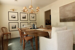 Ein Esszimmer mit Holztisch, Stühlen, gerahmten Bildern an der Wand und einem Kronleuchter.