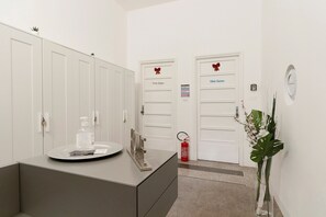 Een hotelkamer met een grijze dressoir, een kleine plant, een brandblusser en twee deuren met de aanduiding 'Polo Guía' en 'White House'.