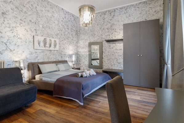 Een slaapkamer met een bed, een bank, een bureau, een kledingkast en een kroonluchter.