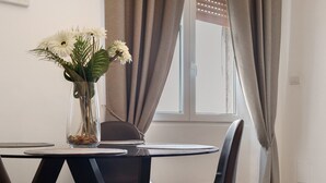 A dining table with a vase of flowers, a chair, and a window with curtains. - Apartment 'Home Experience - Perla Grigia' with Air Conditioning (Bari)