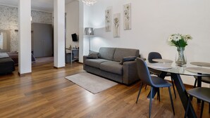 A modern living room with a grey sofa, a glass dining table, and a chandelier. - Apartment 'Home Experience - Perla Grigia' with Air Conditioning (Bari)