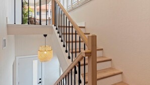 Una escalera de madera con balaustres negros que conduce a un rellano con una puerta blanca y un aplique colgante.