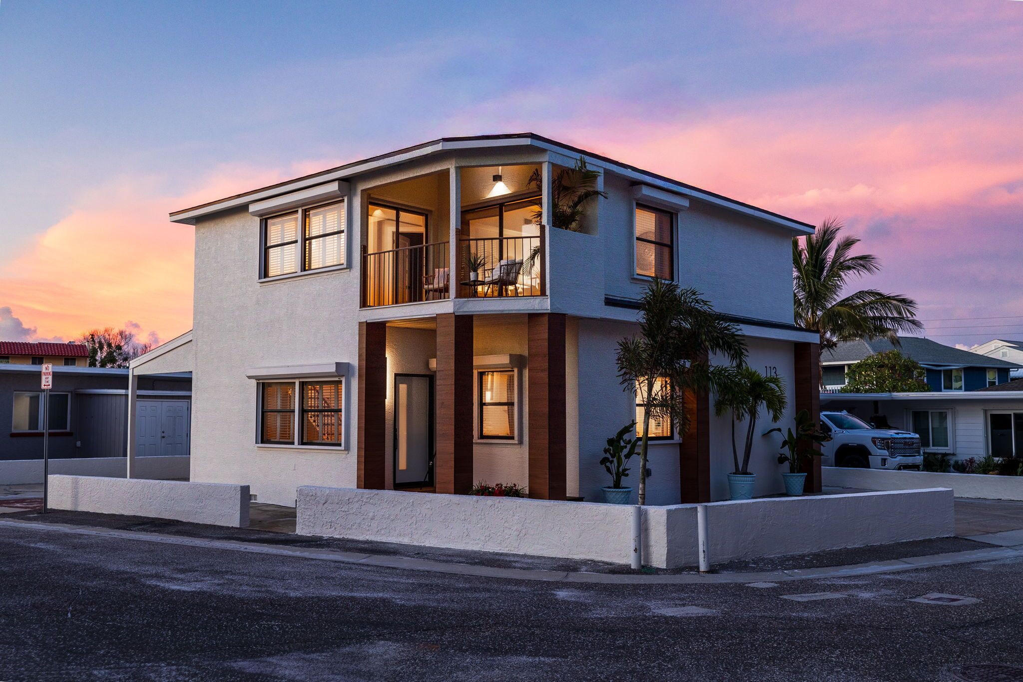A modern two-story house with a balcony, large windows, and a driveway.