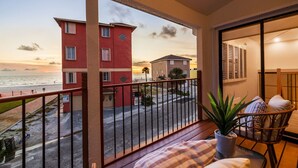 Un balcón con vista a la playa y edificios, una planta en maceta y una silla de mimbre.