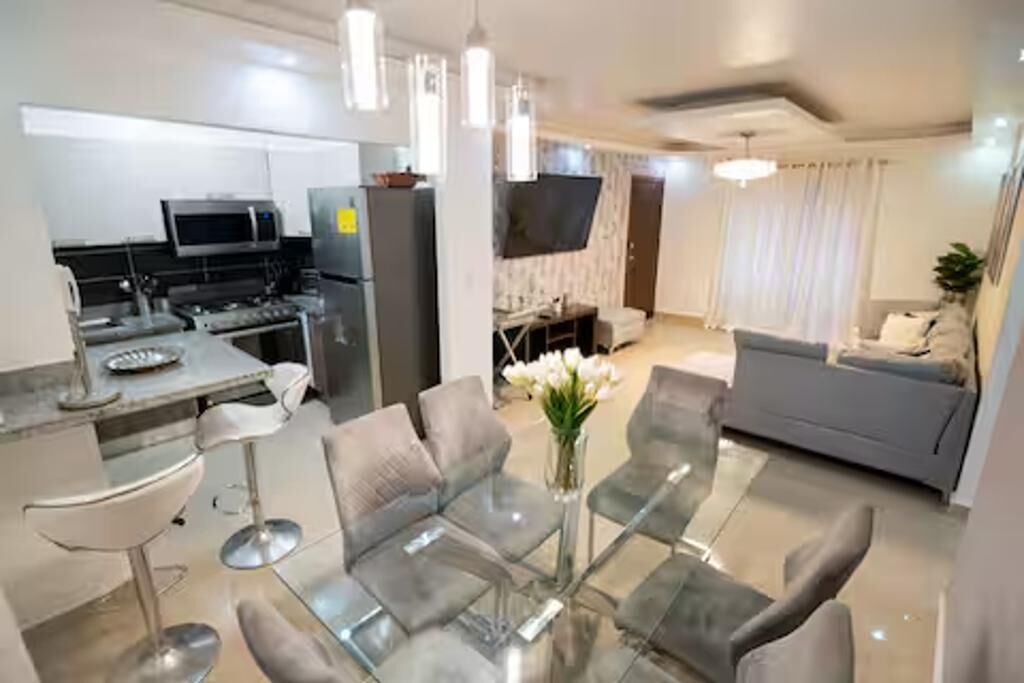 Uma sala de estar moderna com uma mesa de centro de vidro, sofás cinzentos e uma televisão de tela plana.