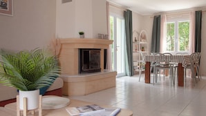 A living room with a fireplace, a dining area with chairs, and a view through a window.