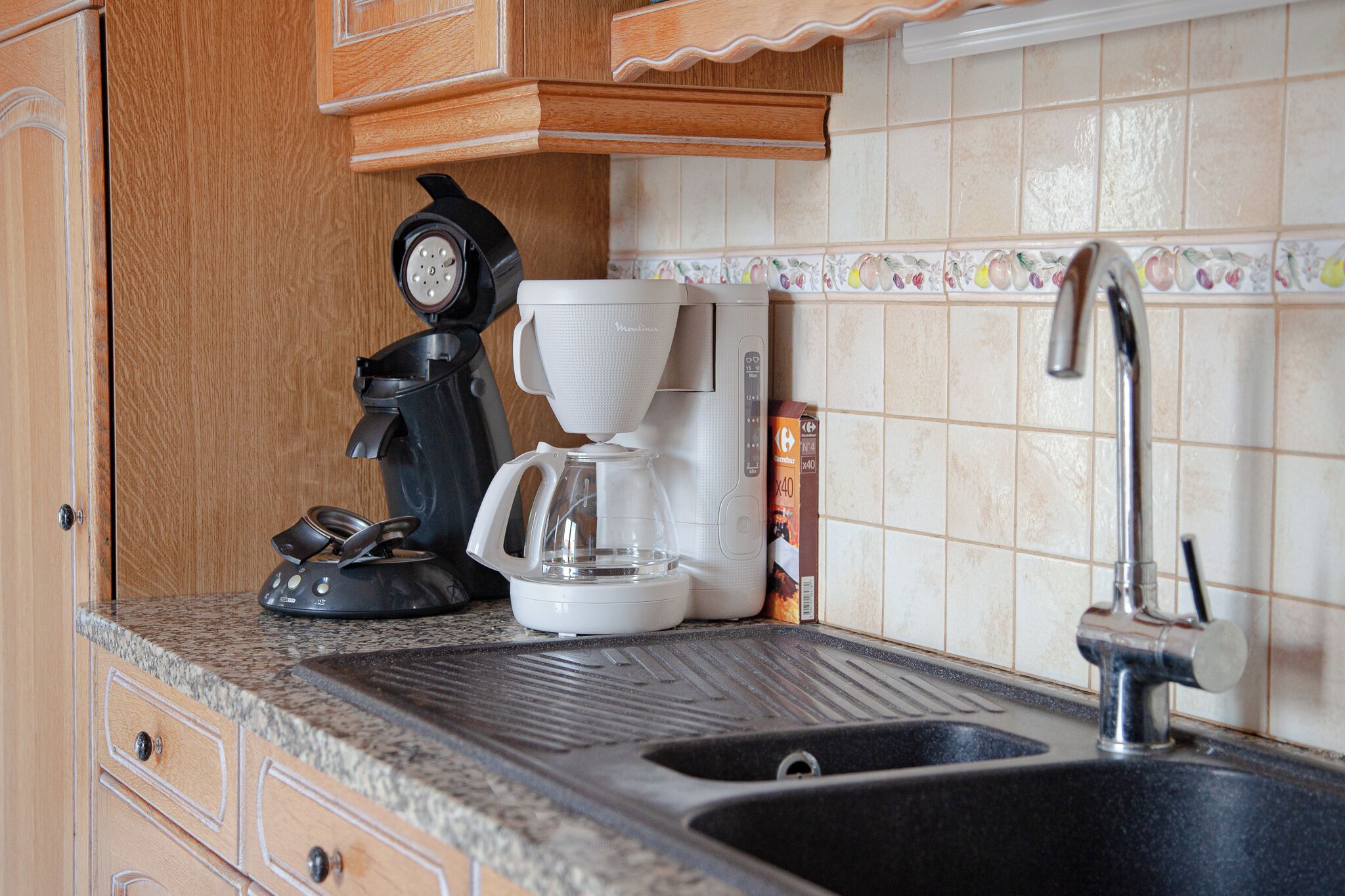 A kitchen with a coffee maker, a kettle, and a sink.