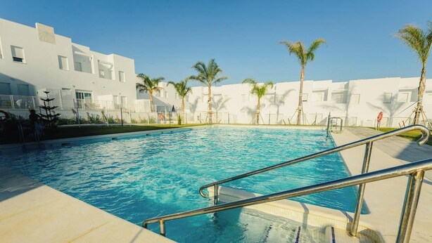 Una piscina con ringhiera metallica, circondata da edifici bianchi e palme.