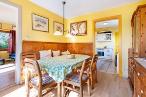 Un coin repas avec une table et des chaises en bois, une nappe à motifs et une vue sur la cuisine.