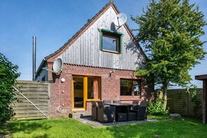 Une maison avec un toit en pente, une antenne parabolique, une façade en briques, une porte en bois et un patio aménagé avec du mobilier d’extérieur.