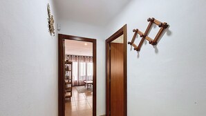 A hallway with a wooden door, a small shelf with decorative items, and a wall-mounted wooden frame. - LA SOLANA Roses / Roses - INTERimmo (Rosas / Roses)