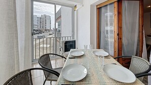 A dining area with a table set for four, chairs, and a view of a cityscape through a glass door. - LA SOLANA Roses / Roses - INTERimmo (Rosas / Roses)