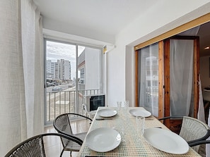 A dining area with a table set for four, chairs, and a view of a cityscape through a glass door. - LA SOLANA Roses / Roses - INTERimmo (Rosas / Roses)
