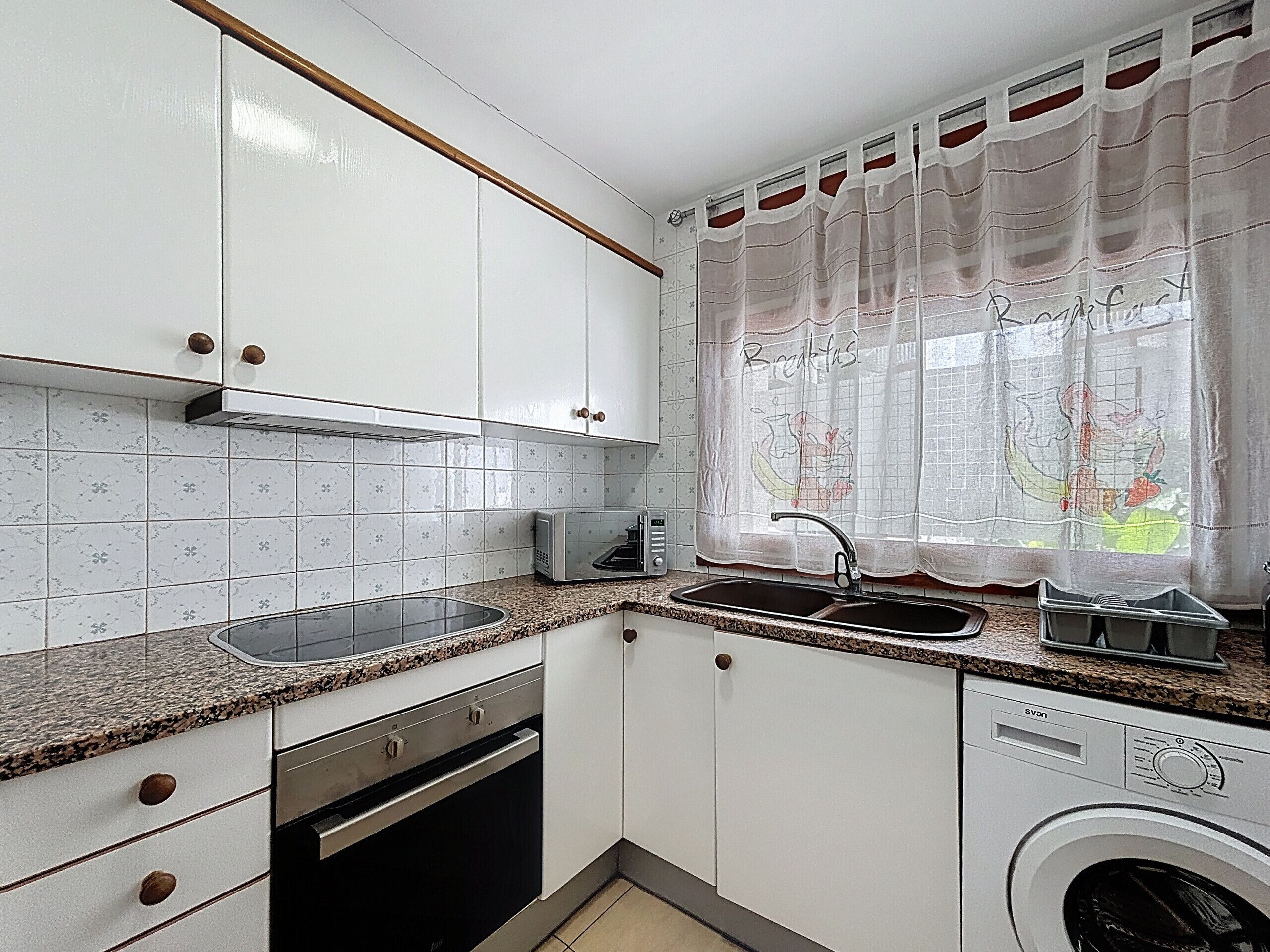 A compact kitchen with white cabinets, a granite countertop, a built-in toaster, a sink, and a front-loading washing machine.