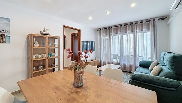 A modern living room with a wooden dining table, a green sofa, and a glass cabinet with kitchenware. - LA SOLANA Roses / Roses - INTERimmo (Rosas / Roses)
