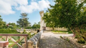 Un chemin de pierre mène à un bâtiment à l’architecture traditionnelle, entouré de verdure et sous un ciel dégagé.