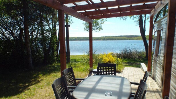 Alpendre coberto com mesa e cadeiras, com vista para um lago.