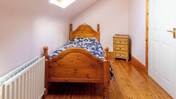 A bedroom with a wooden bed, a small bedside table, a radiator, and a door.