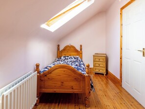 A bedroom with a wooden bed, a small bedside table, a radiator, and a door. - BALLYNEILL FARMHOUSE in Carrick-On-Suir, County Tipperary (Mullagh)