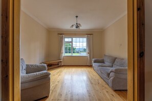 A spacious room with a wooden floor, two sofas, a bench, and a window with curtains. - BALLYNEILL FARMHOUSE in Carrick-On-Suir, County Tipperary (Mullagh)