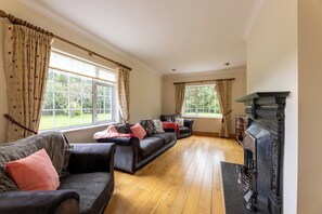 A spacious living room with two sofas, a fireplace, and large windows offering a view of greenery.