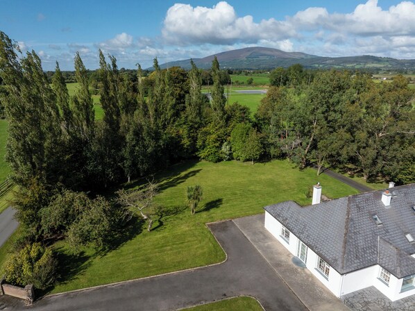 A white house with a grey roof, surrounded by a well-maintained lawn and dense trees. - BALLYNEILL FARMHOUSE in Carrick-On-Suir, County Tipperary (Mullagh)