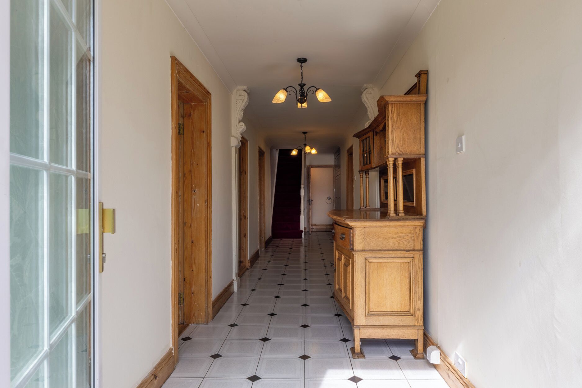 A hallway with a wooden cabinet and a chandelier.