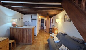 Une cuisine compacte avec des meubles en bois, un coin repas avec une table et des chaises, et un salon avec un canapé.
