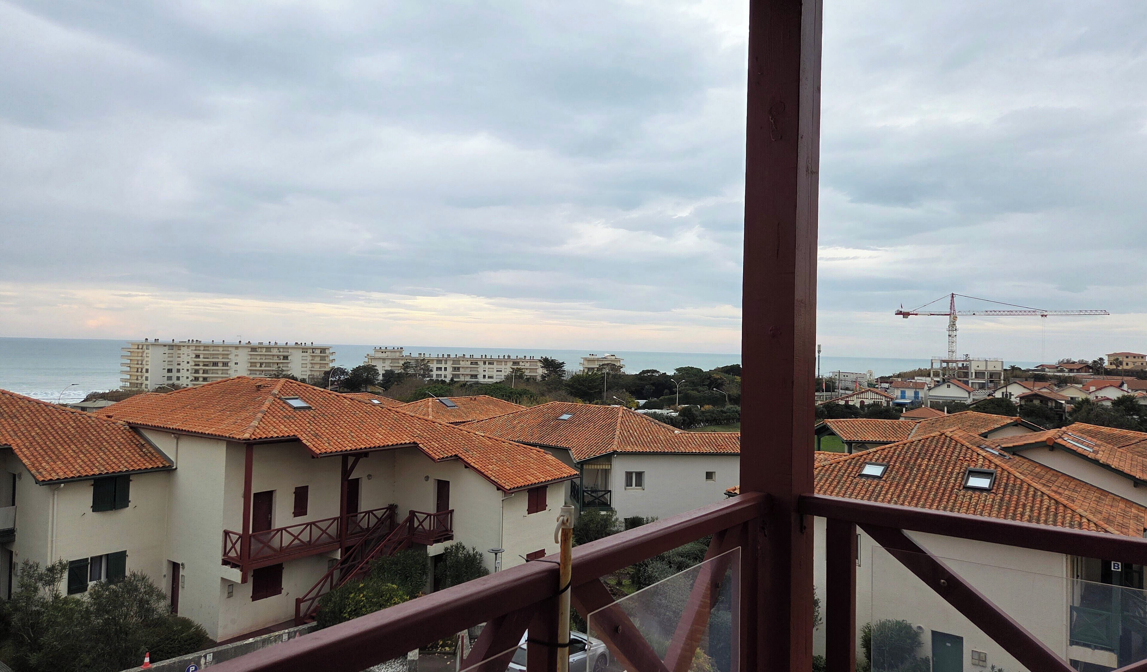 Un quartier résidentiel situé sur la côte, avec des toits recouverts de tuiles en terre cuite, une vue sur la mer et une grue de construction visible au loin.
