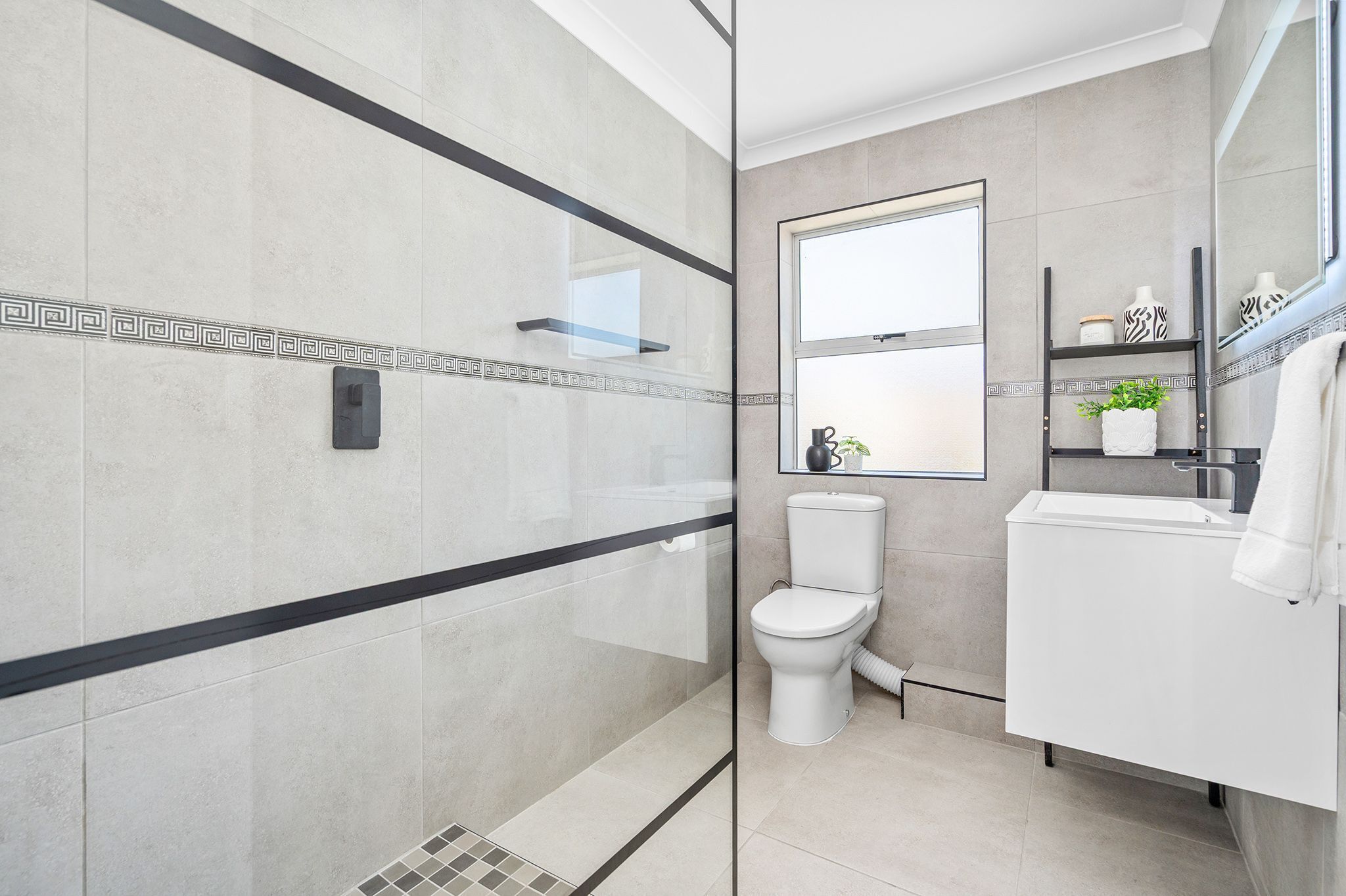 A modern bathroom with a glass shower enclosure, a toilet, and a sink with a mirror.
