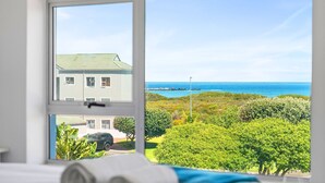 Una habitación con un ventanal grande que da a un paisaje costero, incluyendo un edificio y vistas al océano.