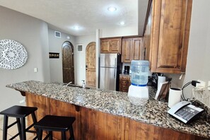 Eine Küche mit Granit Arbeitsplatten, Holzschränken, einem Edelstahlkühlschrank und einem Wasserspender.