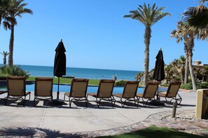 Un espace aménagé au bord de la piscine, avec des chaises longues et des parasols, offrant une vue sur un océan d’un bleu limpide.