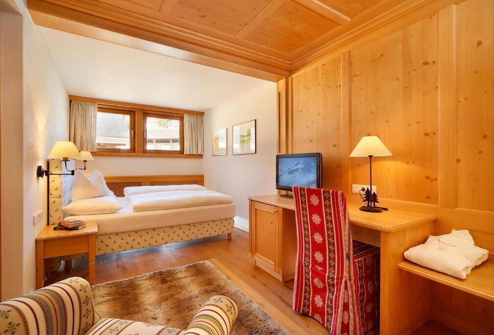 A cozy room with a bed, a television, a desk, and a window.