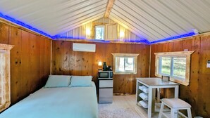 A cozy cabin bedroom with a bed, a desk, a chair, and a small kitchenette.