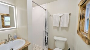 A bathroom with a wooden vanity, a white sink, a shower with a glass door, a toilet, and two white towels hanging on the wall.