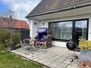 Een terras met een tafel en stoelen, een barbecue en een overdekte zithoek met een bord.