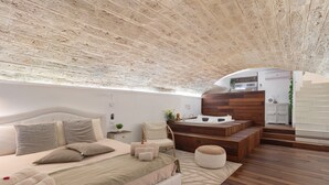 A modern bedroom with a large bed, a wooden bench, a small table, and a built-in kitchen area. - 'Lc Luxury' Apartment with Wi-Fi and Air Conditioning (Bari)