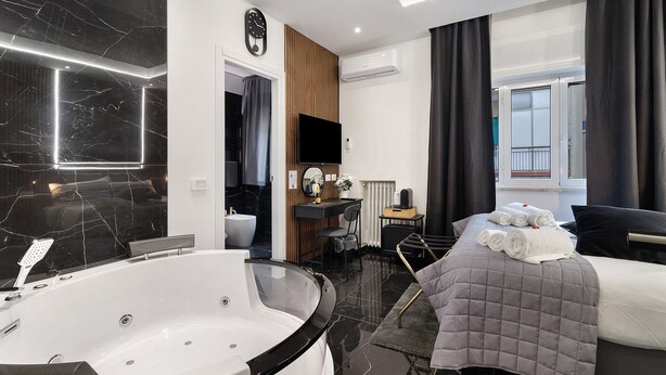 A modern hotel room with a large bathtub, a bed with a quilted cover, a desk with a chair, and a view of the outside. - 'Salandra' Room with Wi-Fi and Air Conditioning (Bari)