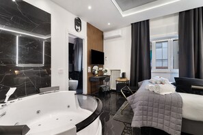 Een moderne hotelkamer met een groot bad, een bed met een gebogen sprei, een bureau met stoel, en uitzicht naar buiten.