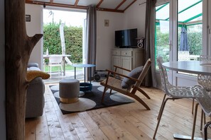 A room with a wooden floor, a sofa, a rocking chair, a small table, a TV, and a cabinet.