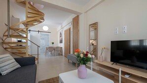 Ett modernt vardagsrum med en spiraltrappa, en platt-TV, en soffa och ett soffbord med en vas med blommor.